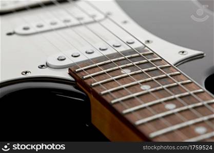 Electric guitar, closeup view on wooden fretboard, black background, nobody. String musical instrument, electro sound, electronic music, equipment for stage concert. Electric guitar, closeup view on wooden fretboard