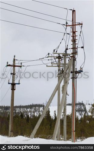 Electric line on concrete piers with reclosers on the background of snow-covered forest
