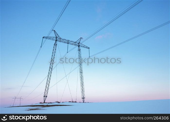 Electric power line in empty winter field at pastel sunset