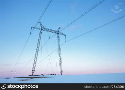 Electric power line in empty winter field at pastel sunset