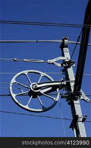 Electric railway steel wires infrastructure over vivid blue sky, wheel.