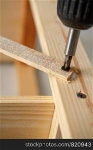 Electric screwdriver twists screw in a wooden structure close-up. screwdriver tightens the screw