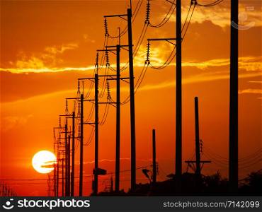 Electric tower silhouetted on sunset time background.Line of electricity poles arranged in order to distribute electric power to the community source.