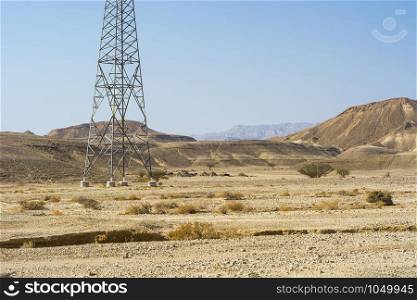 Electrical power lines on pylons in the landscape of the Middle East. Rocky hills of the Negev Desert in Israel. Breathtaking landscape of the rock formations.