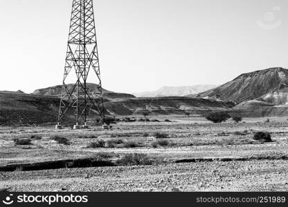 Electrical power lines on pylons in the landscape of the Middle East. Rocky hills of the Negev Desert in Israel. Breathtaking landscape of the rock formations. Black and white photography