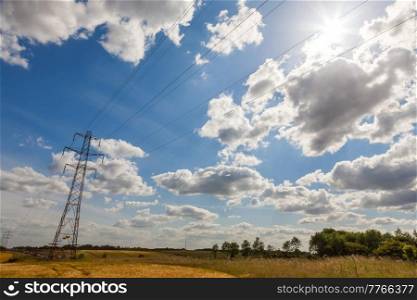 Electrical pylon power lines and traffic cars queuing on a motorway or freeway with blue sky clouds and sunshine