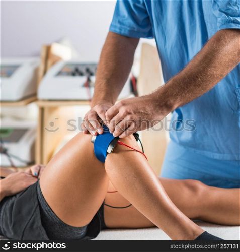 Electrical stimulation in physical therapy. Therapist positioning electrodes on a patient&rsquo;s knee