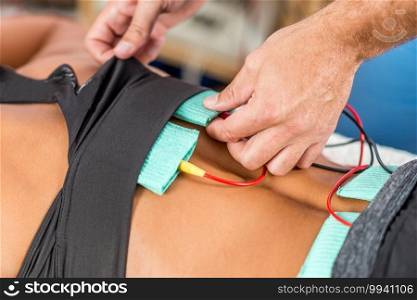 Electrical stimulation in physical therapy. Therapist positioning electrodes onto a female athlete’s lower back muscles