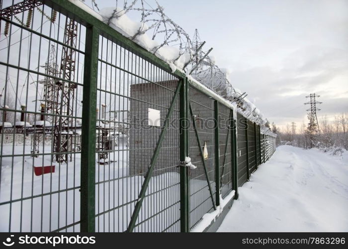 electrical substation behind a fence topped with barbed wire. Winter