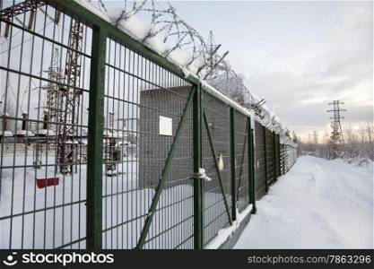 electrical substation behind a fence topped with barbed wire. Winter