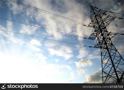 electrical tower with bright sun, blue sky and white clouds