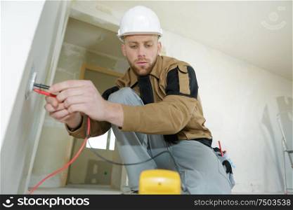 electrician checking socket voltage using multimeter in a wall fixture