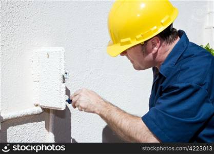 Electrician doing repairs inside and electrical box on the outside of a home. Model is a licensed electrician and all work is being performed according to industry code and safety standards.