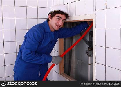 Electrician feeding red pipe behind a tiled wall