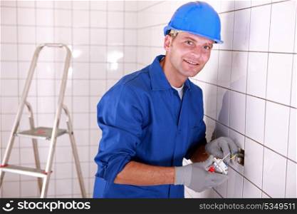 Electrician fitting a light switch in a large white tiled room