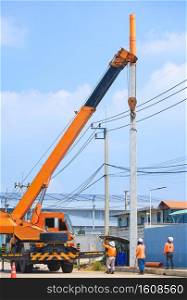 Electrician group with crane truck is lifting new electrical pole to installing on roadside in industrial settlement area