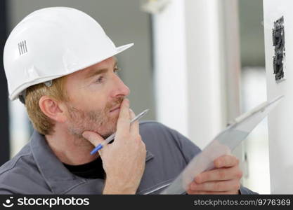 electrician holding clipboard inspecting installation on wall