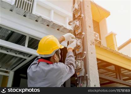 Electrician in a gray uniform wears gloves and a helmet installing a power meter on an electricity pole.