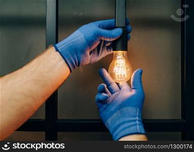 Electrician in uniform replaces the light bulb, handyman. Professional worker makes repairs around the house, home repairing service. Electrician changes the light bulb, handyman