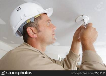 electrician installs lighting to the ceiling in the office