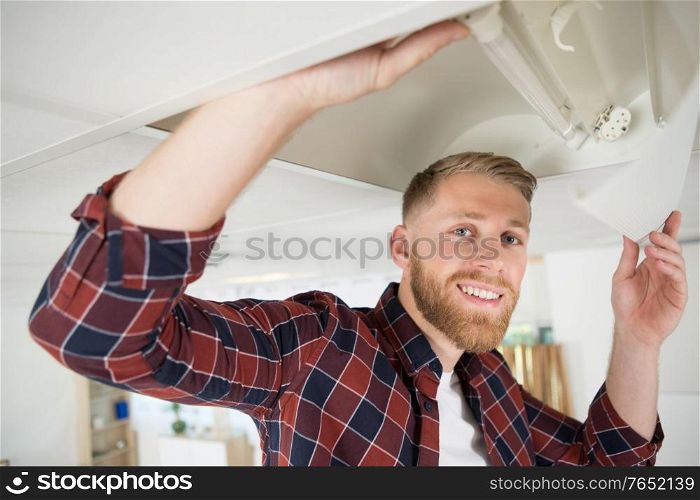 electrician man worker in uniform installing ceiling fluorescent lamp