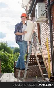 Electrician standing on high stepladder and holding plan of house