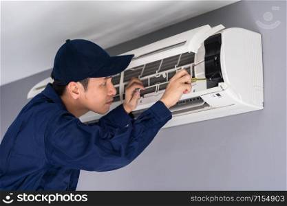 Electrician with screwdriver repairing the air conditioner indoors