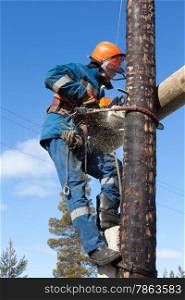 Electrician working on electricity pylon chainsaw against the blue sky