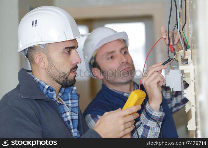 electricians checking socket voltage with digital multimeter two workers