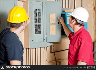 Electricians examining a circuit breaker panel in an industrial setting.