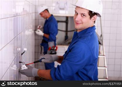 Electricians wiring a large white tiled room