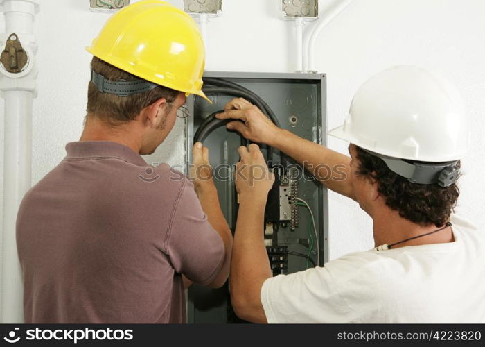 Electricians working together to install a breaker panel. Models are actual electricians - all work is performed according to industry standard code and safety practices.