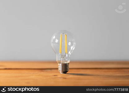 electricity, energy and power consumption concept - close up of lightbulb on wooden table. close up of lightbulb on wooden table