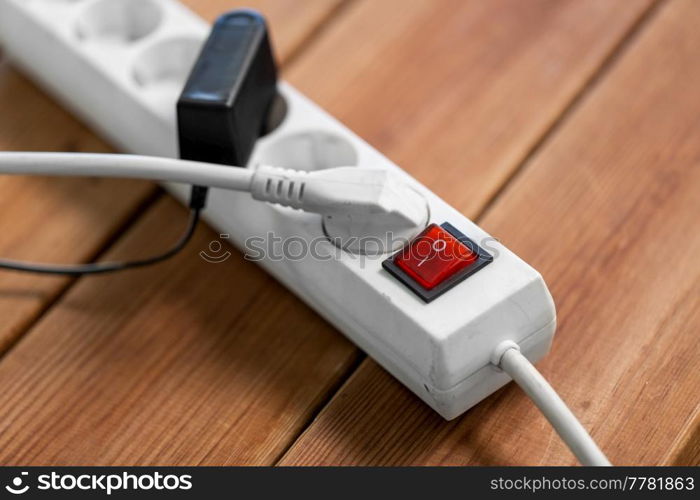 electricity, energy and power consumption concept - close up of socket with plugs, charger and red switch button on wooden floor. close up of socket with plugs and charger on floor