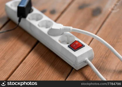 electricity, energy and power consumption concept - close up of socket with plugs, charger and red switch button on wooden floor. close up of socket with plugs and charger on floor