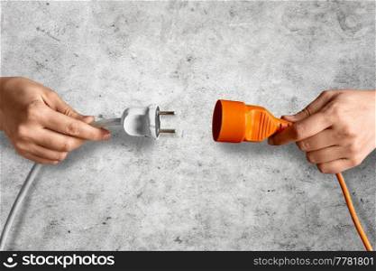 electricity, energy and power consumption concept - close up of woman inserting plug into socket over concrete background. close up of woman inserting plug into socket