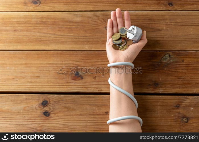 electricity, energy crisis and power consumption concept - close up of hand wrapped with plug holding coins on wooden table. close up of hand wrapped with plug holding coins