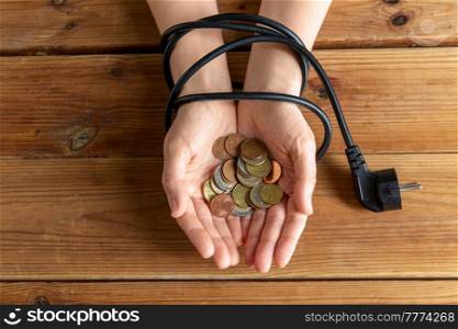 electricity, energy crisis and power consumption concept - close up of hands tied with plug holding coins on wooden table. close up of hands tied with plug holding coins