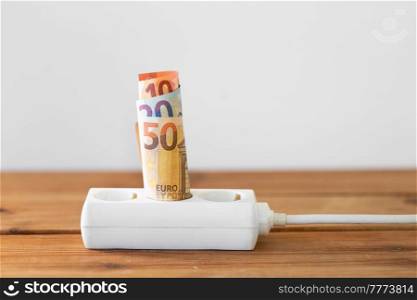 electricity, energy crisis and power consumption concept - close up of money inside electric socket. close up of money inside electric socket