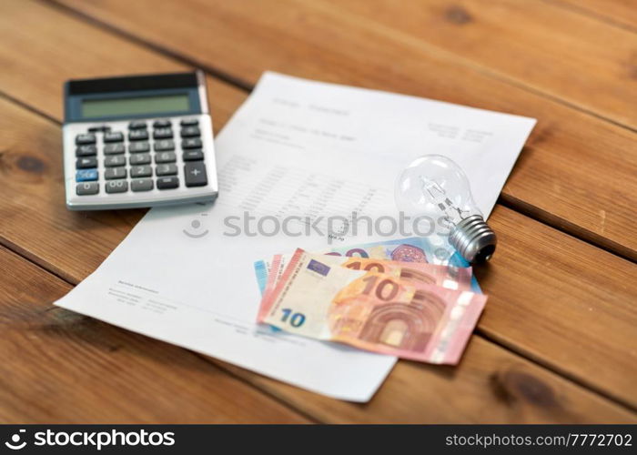 electricity, energy crisis and power consumption concept - close up of utility bill, calculator, money and lightbulb on wooden table. utility bill, calculator, money and lightbulb