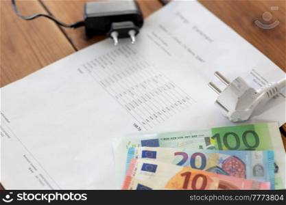 electricity, energy crisis and power consumption concept - close up of utility bill, money and electric plugs on wooden table. utility bill, money and electric plugs on table
