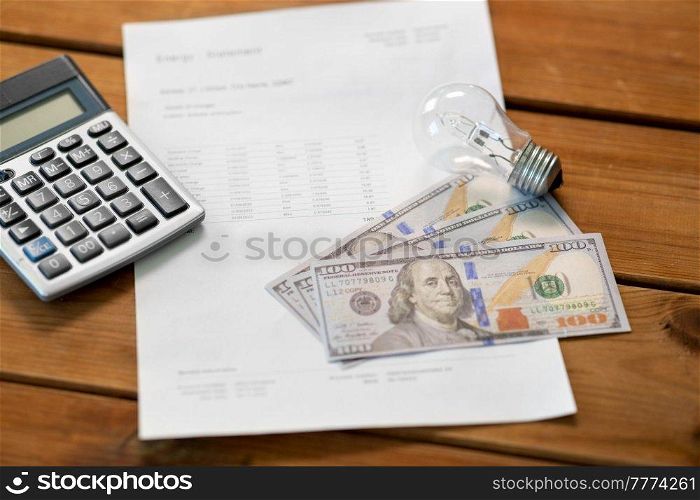 electricity, energy crisis and power consumption concept - close up of utility bill, calculator, money and lightbulb on wooden table. utility bill, calculator, money and lightbulb