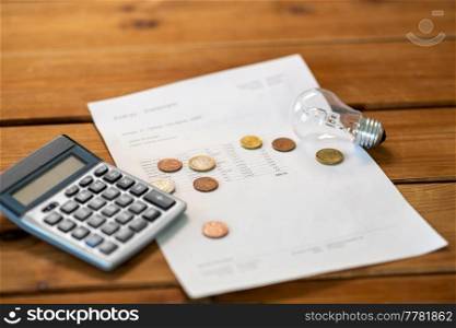 electricity, energy crisis and power consumption concept - close up of utility bill, calculator, money and lightbulb on wooden table. utility bill, calculator, money and lightbulb