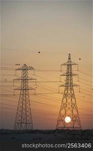 Electricity Pylons Silhouetted At Sunset