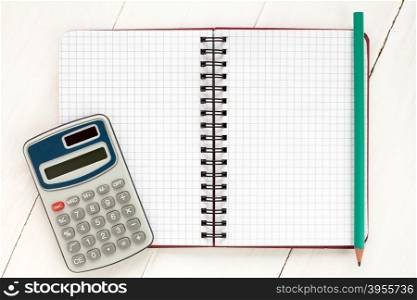 Electronic calculator and spiral notebook on the white wooden background