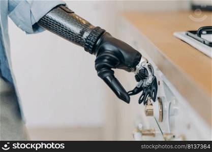 Electronic cyber hand of disabled person is switching a stove on at kitchen. Amputee with high technology carbon arm. Sensor in fingers and wrist joint. Daily routine of disabled.. Electronic cyber hand of disabled person is switching a stove. Sensor in fingers and wrist joint.