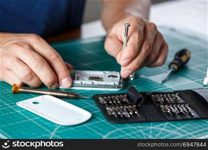 Electronics repair service. Technician disassembling smartphone for inspecting.. Electronics repair service. Technician disassembling smartphone for inspecting