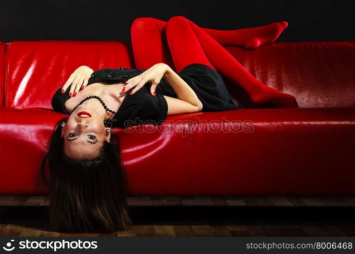 Elegance and fashion outfit. Fashionable woman legs in red vivid color tights posing on couch black background