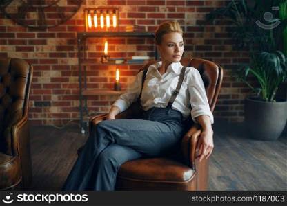 Elegance business woman in strict clothes poses on leather couch in studio, retro fashion, gangster style, mafia.. Elegance woman in strict clothes, gangster style