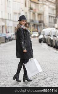 elegant and cute woman , in the middle of a road , with shopping bag for winter sale , she is wearing voat and a nice hat